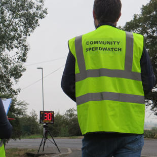 Speedwatch volunteers stood with their backs to camera in front of a digital display showing 30
