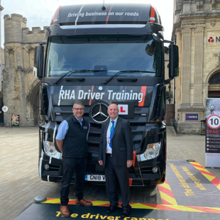 Two men standing in front of a Heavy Goods Vehicle that is surrounded by blind-spot mats.