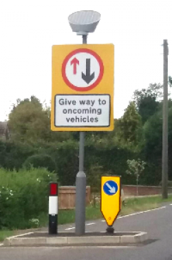 Give way to oncoming vehicles sign and bollards on a road narrowing