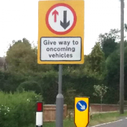 Give way to oncoming vehicles sign and bollards on a road narrowing