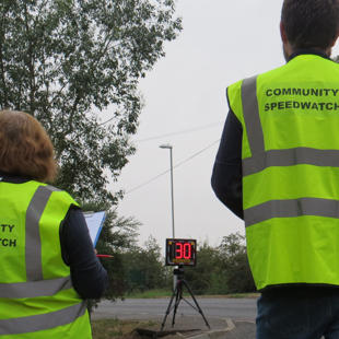 Speedwatch volunteers stood with their backs to camera in front of a digital display showing 30